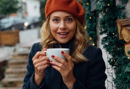 Koffieliefhebber: vrouw met kop koffie in haar handen, op de achtergrond kerstversiering buiten