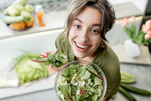 Vrouw eet salade in de keuken thuis