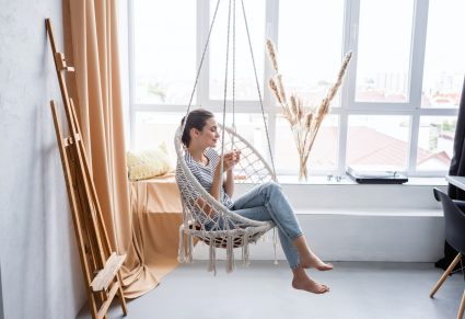 vrouw zit bij het raam in een macrame hangstoel