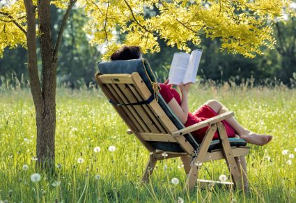 vrouw zit buiten op een tuinstoel en leest een boek