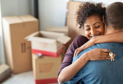 Dromen Over Verhuizen: vrouw omhelst man met verhuisdozen op achtergrond