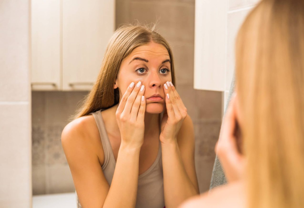 vrouw bekijkt haar wallen in de spiegel