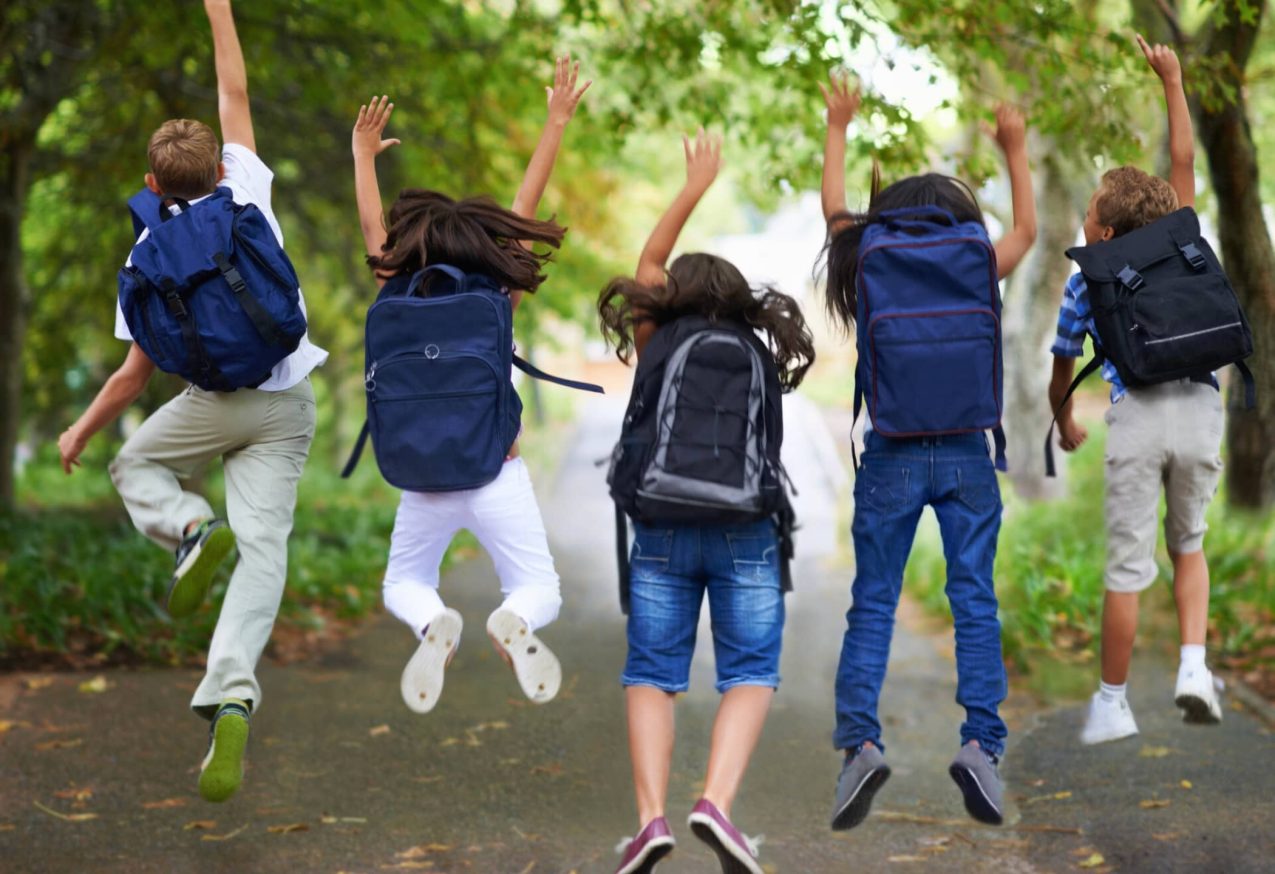 Back To School Checklist: Achteraanzicht van vijf kinderen die met rugzakken in de lucht springen