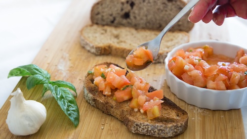 bruschetta recept: persoon doet bruschetta op een broodje