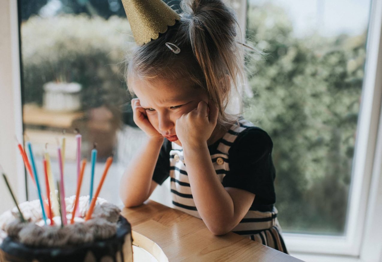 Kleuter Blijft Zeuren: meisje met feestmuts kijkt boos naar een verjaardagstaart