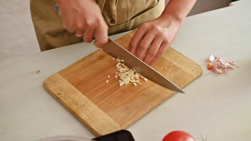 patatas bravas voorbereiding: Close-up van persoon die knoflook hakt op houten snijplank