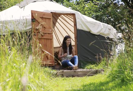 Vrouw zit bij ingang van een yrt tent, in de natuur