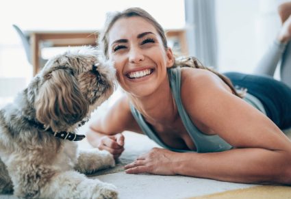 Honden Duwen Snuit Tegen Je Aan: vrouw in sportkleding, ligt oop vloer met hond die zijn snuit tegen haar gezicht duwt