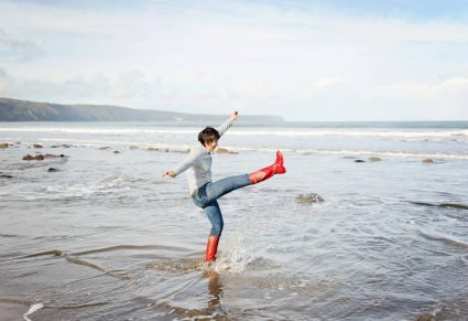 Regenlaarzen: vrouw schopt water weg in zee met regenlaarzen aan