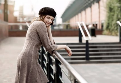 Gebreide Jurken: Portret van jonge vrouw met baret en gebreide jurk leunend op een reling