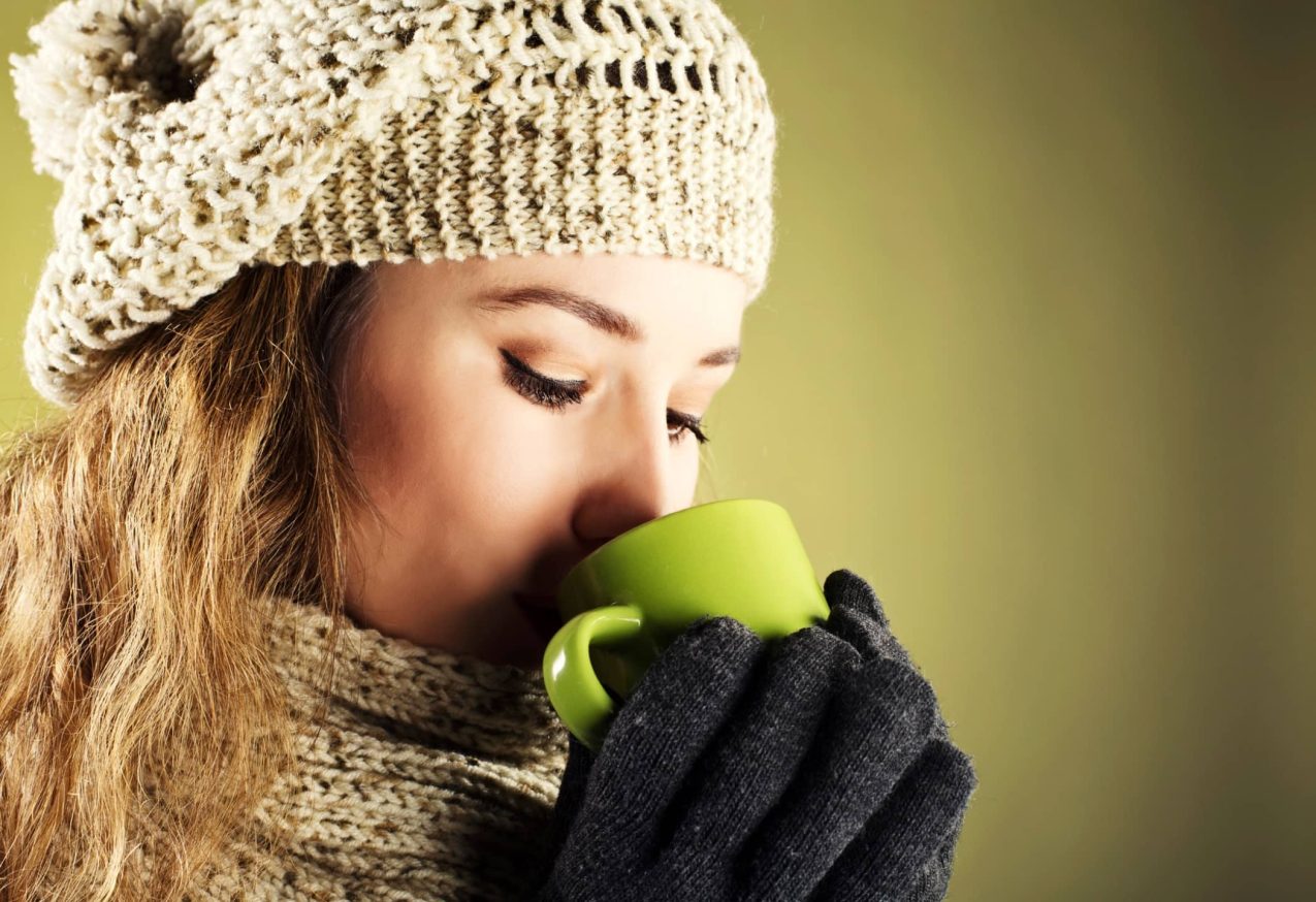 Nooit Meer Koud: Jonge en mooie vrouw met muts op en handschoenen aan die koffie drinkt