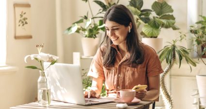 Positive Young Mixed Race Woman Using A Laptop And Smartphone At Home.cozy Home Interior With Indoor Plants.remote Work, Business,freelance,online Shopping,e Learning,urban Jungle Concept