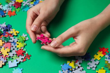 Puzzelen: Gekleurde puzzels in handen op groene achtergrond