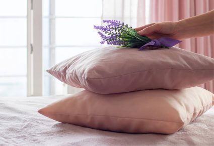 Rustgevende Geur: hand die bosje lavendel bovenop gekleurde kussens op bed legt.