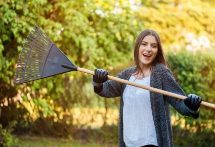 Tuin Winterklaar Maken: Lachende jonge vrouw met tuin blad hark in haar eigen achtertuin