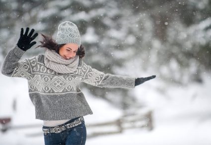 Winteroutfits: mooie vrouw in de sneeuw met trui en jeans aan