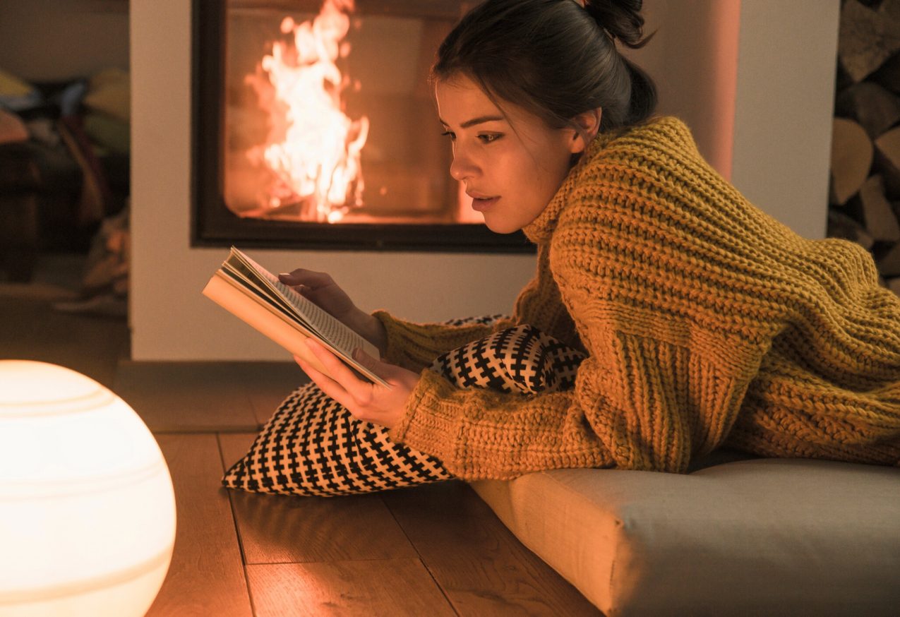 Waargebeurde Verhalen: Jonge vrouw leest boek bij de open haard thuis