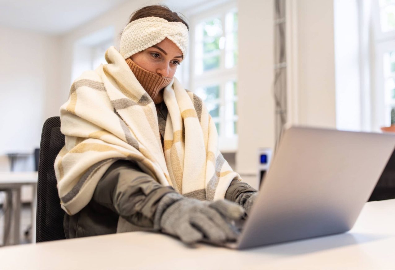 Warme Werkplek Met Verwarmingspaneel Action: vrouw met handschoenen aan en kleed om achter laptop