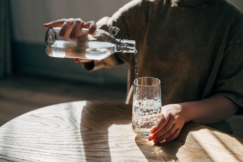 Een vrouw aan tafel schenkt een glas water uit een fles