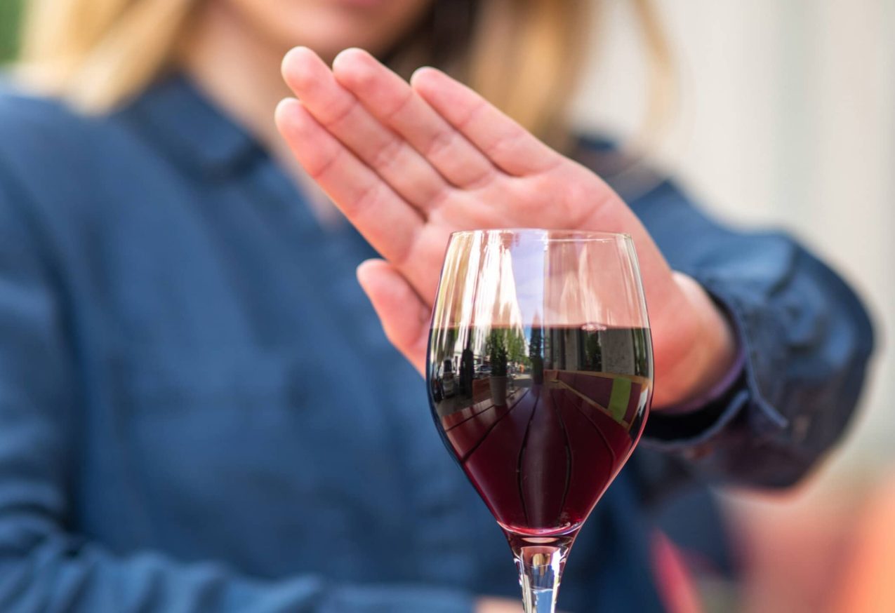 Dry January: Een vrouw aan tafel gebaart met haar hand om een glas rode wijn te weigeren