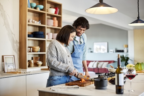 Lachende man kijkt naar vrouw die wortel hakt. Gelukkig stel kookt thuis samen eten. Ze zijn in de keuken | fases van liefde