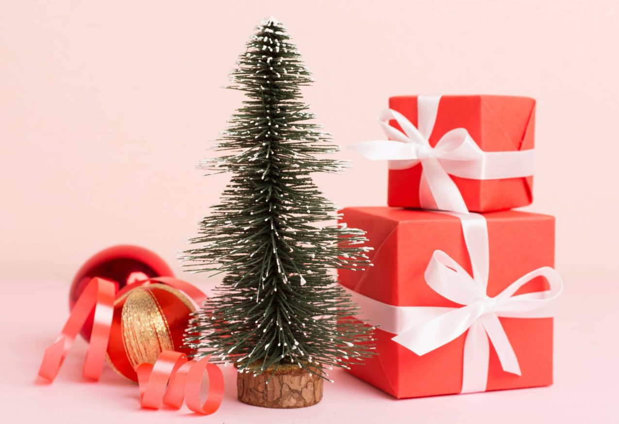 miniatuur kerstboompje met kerstcadeautjes, roze achtergrond: originele woonaccessoires