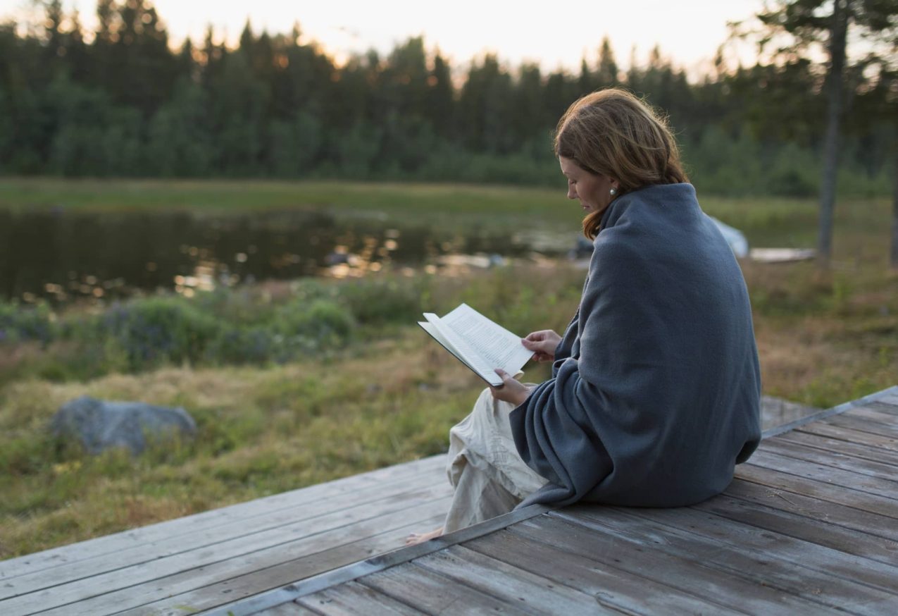 Boeken Over Woii: vrouw leest boek op terras, met als achtergrond bos en grauw weer