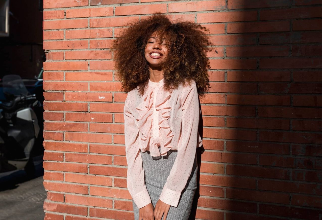 Trendy Blouses: mooie vrouw leunend tegen een muur met roze blouse aan